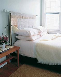 a bed with white sheets and pillows next to a wooden table in front of a window