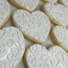 many heart shaped cookies are arranged on a counter top with white icing and swirly decorations