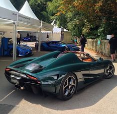 a green sports car parked in front of a white tent with people standing around it