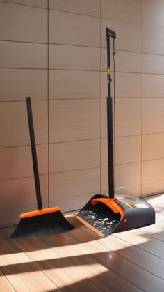 an orange and black snow shovel sitting on top of a hard wood floor next to a wall