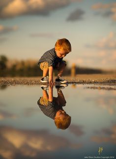 a little boy playing with his reflection in the water