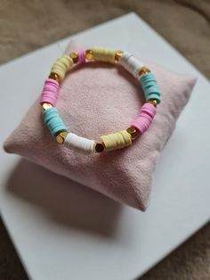 a pink and blue beaded bracelet sitting on top of a white pillow next to a cushion