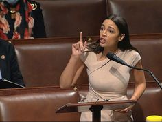 a woman standing in front of a microphone giving a peace sign while another man stands behind her