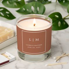 a candle sits next to some matches on a marble table with greenery in the background