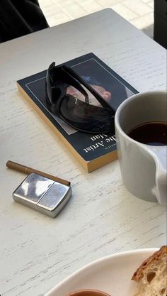 a cup of coffee next to a book and cell phone on a white table top