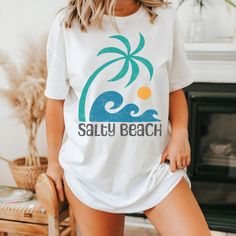 Embrace island vibes with our Salty Beach retro summer shirt featuring a tropical palm tree and wave graphic, reminiscent of vintage surf culture.  The graphic on this shirt is faded and distressed to create a vintage look. We use professional quality DGT printing on all our apparel. Direct-to-garment, or DTG, is a high quality printing method that sprays ink directly onto the garment so there is no peeling or cracking. This fabulous graphic will be printed on a Comfort Colors Unisex T-Shirt. Pl Tropical Graphic Print T-shirt For Beach, Funny Print T-shirt For Beach Vacation, White Tropical T-shirt For Beach Season, Relaxed Fit Beachy Hawaiian Shirt For Vacation, Relaxed Fit Tropical Tops For Beach, Cotton Tropical Tops For Beach Season, Trendy Hawaiian Shirt For Vacation, White Vacation Tops With Palm Tree Print, Trendy Short Sleeve Hawaiian Shirt For Vacation