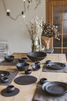 a wooden table topped with black plates and bowls next to a vase filled with flowers