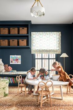 three children sitting at a white table in a blue room with bookshelves on the wall