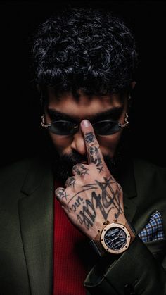 a man with tattoos on his arm and hand in front of his face, wearing a suit