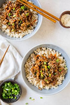 two bowls filled with rice and meat next to chopsticks on a white surface