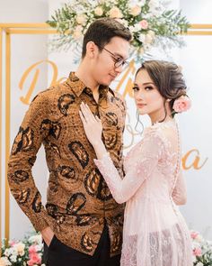 a man and woman standing next to each other in front of a floral wallpaper