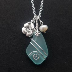 a sea glass pendant with shells and pearls on a black background, hanging from a silver chain