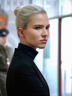 a woman with blonde hair is standing in front of an officer and looking off into the distance