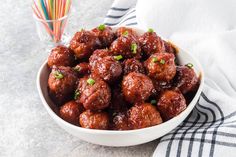 a white bowl filled with meatballs on top of a table next to a straw