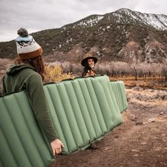 a woman holding an inflatable mattress while standing next to a man wearing a hat