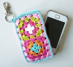 a crocheted cell phone case sitting on top of a table next to a smart phone