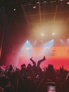 a crowd of people at a concert with their arms in the air and one person on stage