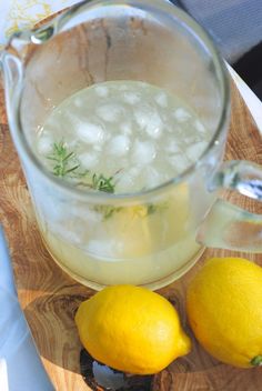 two lemons are sitting on a cutting board next to a pitcher of ice water