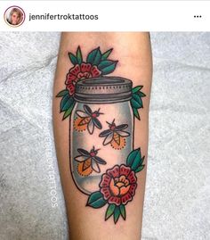 a jar with flowers and bees in it on someone's left leg, next to a tattoo