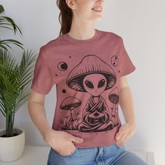 a woman wearing a pink t - shirt with an alien on it and mushrooms in the background