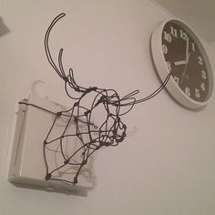 a clock mounted to the side of a white wall next to a wire wrapped deer head