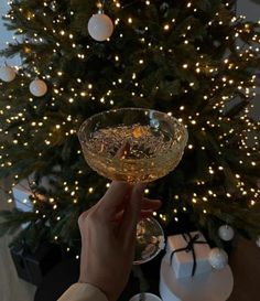 a person holding a wine glass in front of a christmas tree with lights on it