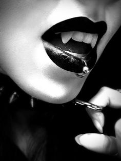 a woman with black lipstick and piercings on her lips is holding a knife to her mouth