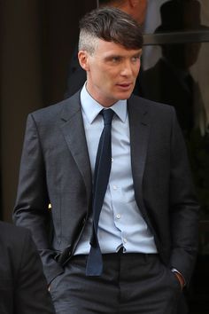 a man in a suit and tie is walking out of a building with his hand on his hip