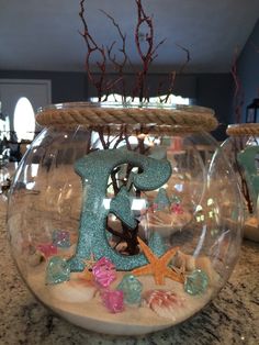 a fish bowl filled with sand and sea shells sitting on top of a marble counter