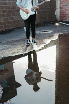 a young man is playing an electric guitar on the street in front of a brick wall