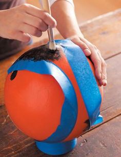 a person is painting an orange, blue and black ball with a brush on it