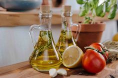 two bottles of olive oil, tomatoes and garlic on a cutting board next to some herbs