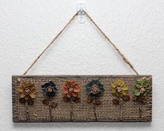 a wooden sign with flowers hanging from it's side on a wall in front of a white wall