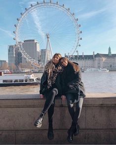 two women are sitting on a ledge in front of the ferris wheel