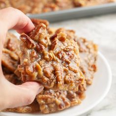 a person is holding up some cookies on a white plate with pecans in the background