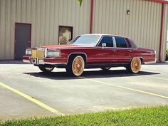 a red station wagon parked in front of a building next to a parking lot with grass