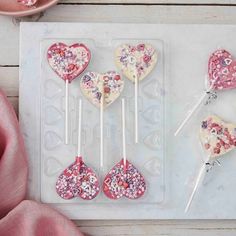 heart shaped lollipops are on a tray with pink and white flowers in them