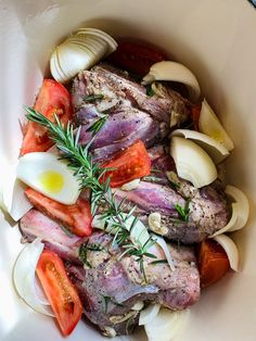 a white bowl filled with meat, onions, and tomatoes on top of a table