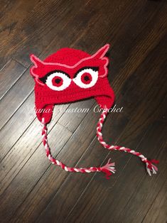 a red crocheted hat with eyes on it sitting on top of a wooden floor