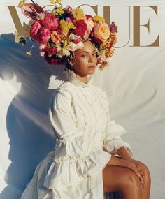 a woman with flowers on her head sitting in front of a white wall wearing a dress