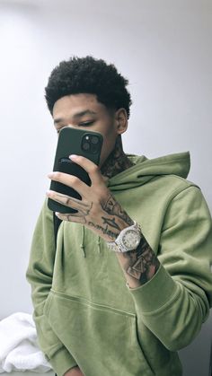 a young man taking a selfie with his cell phone while wearing a green hoodie