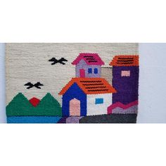 a rug with houses and birds is hanging on the wall in front of a white wall