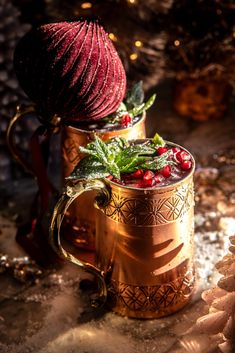 two copper mugs filled with cranberries and greenery on top of snow