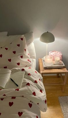 a bed with white sheets and red hearts on it, next to a night stand