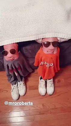 two small dolls are under a bed with sunglasses on their heads and one is wearing an orange shirt