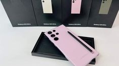 a pink cell phone sitting on top of a black box next to two boxes with pens