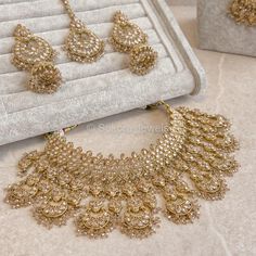 the necklace and earrings are on display in front of a white velvet box with gold trimming