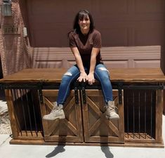 a woman sitting on top of a wooden table next to a garage door and gate