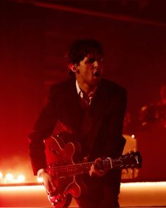 a man in a suit and tie playing an electric guitar on stage at a concert