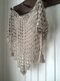 a crocheted shawl hanging from a hook on a white wall with wood slats